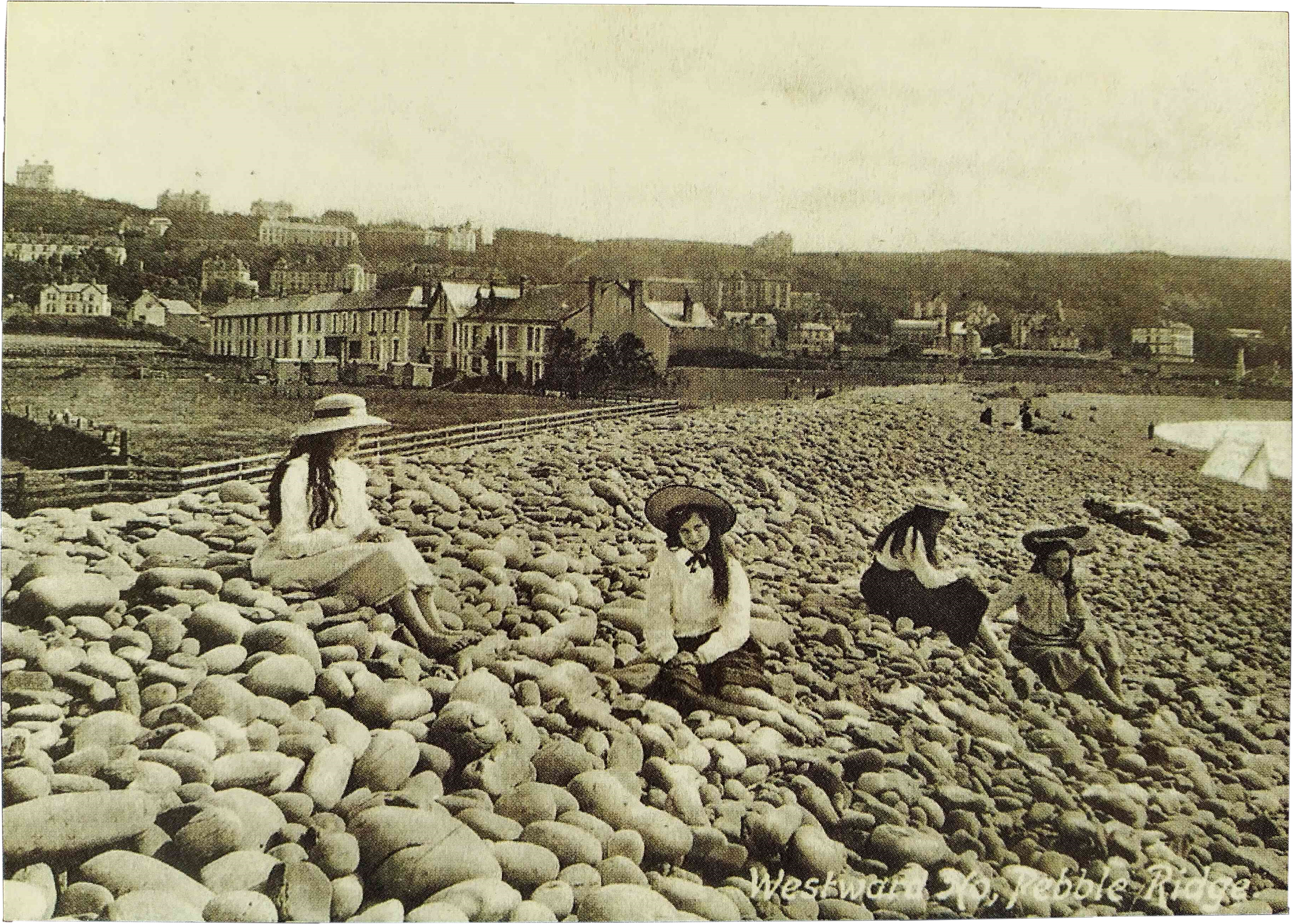 An old black and white photograph of four women and girls in Edwardian clothing sitting on a pebble beach